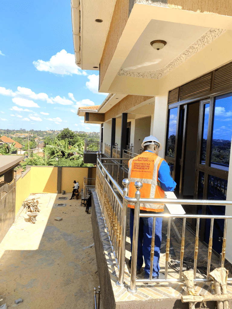 An engineer in Entebbe pointing at structural symbols while teaching a client how to read building blueprints for a new commercial project.