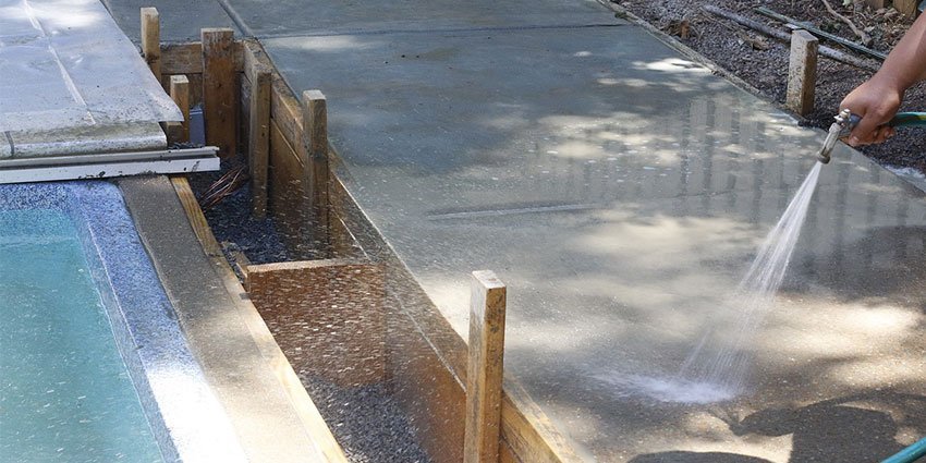 A construction worker in Kampala spraying water on a slab to demonstrate Curing Concrete Why Water Matters.